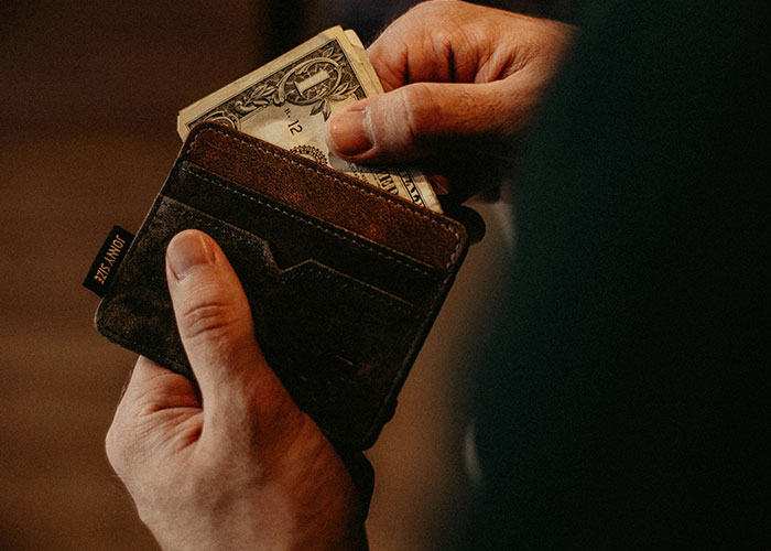 Person holding a brown wallet, pulling out cash, related to parents discovering kids aren’t biologically theirs.