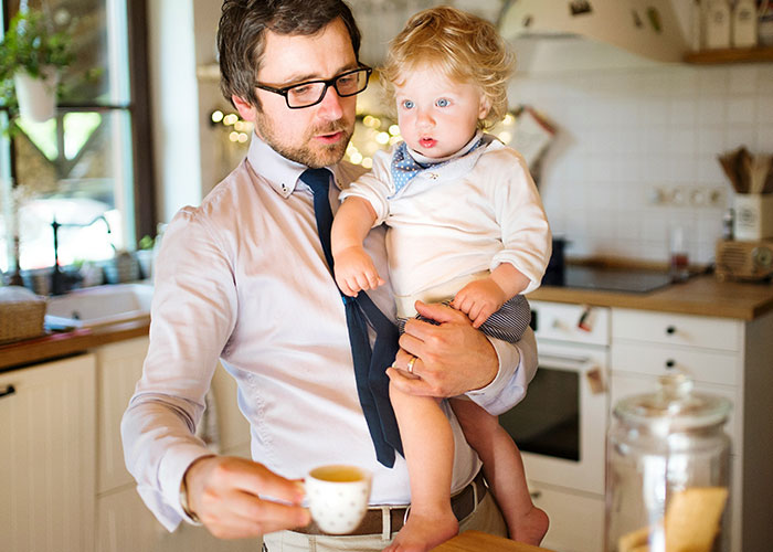 Man holding toddler in kitchen, reflecting on discovering kids were not biologically theirs, showing emotional moment.