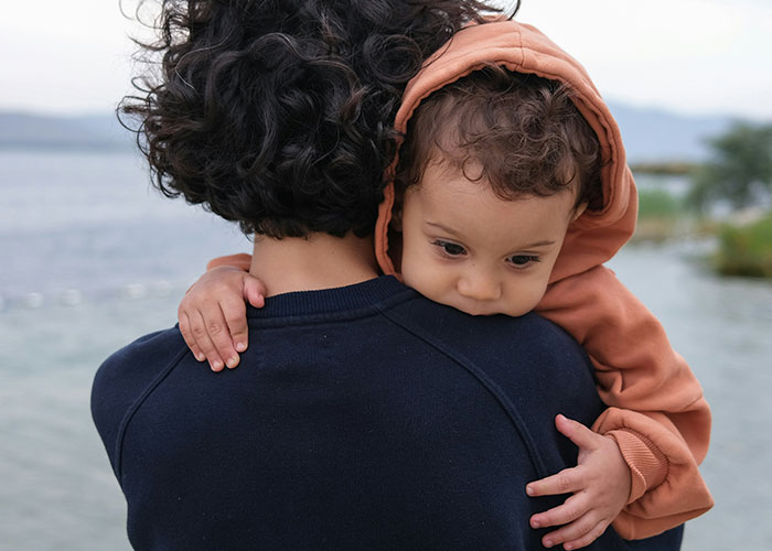 Parent holding young child by water, illustrating emotional moments parents face when kids aren’t biologically theirs.