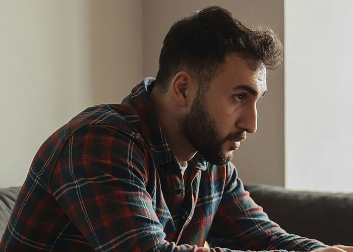 Man in a plaid shirt sitting thoughtfully on a couch, reflecting the emotional impact of discovering kids aren’t biologically theirs