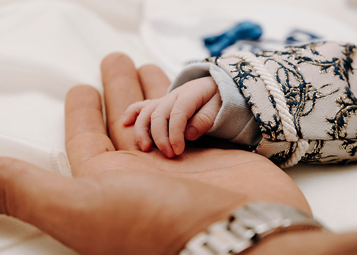 Adult hand gently holding a baby's hand, symbolizing parents discovering their kids weren't biologically theirs.
