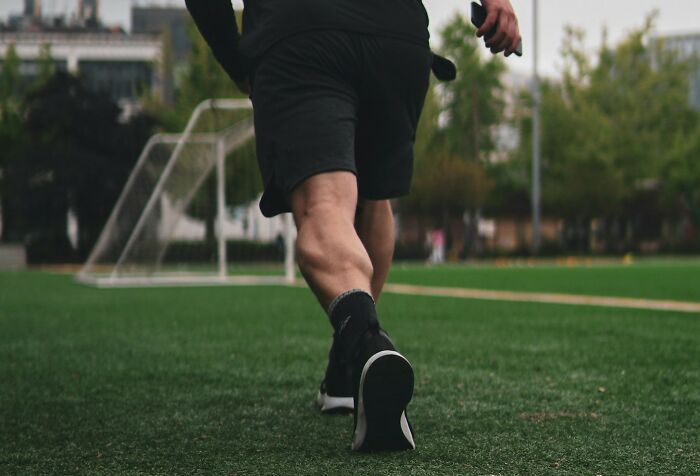 Person walking on a soccer field wearing black shoes and shorts, illustrating the theme of good or bad genes.