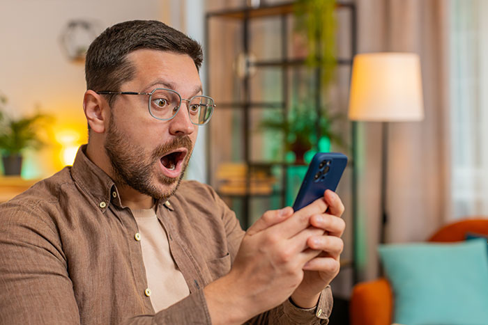 Man with glasses looking shocked at phone screen, illustrating reaction to date changed last minute wedding shaming.