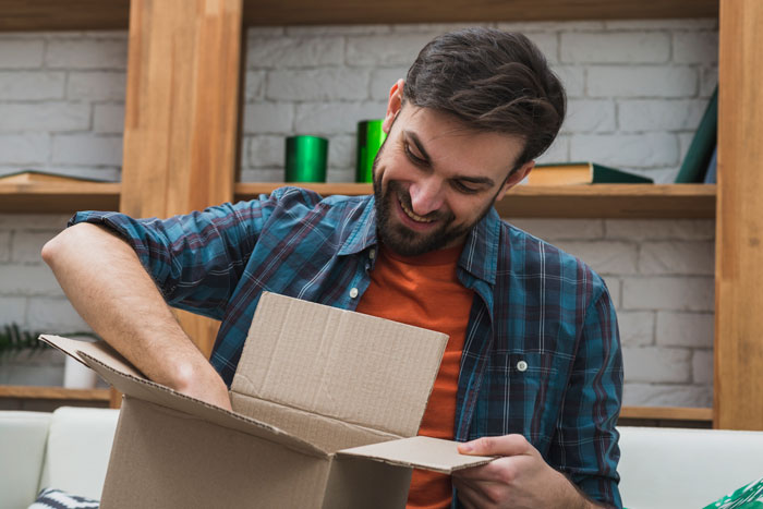 Man smiling while unpacking a cardboard box at home, representing a first date interaction with no spark and meal payment issue. Man smiling while unpacking a cardboard box at home, representing a first date interaction with no spark and meal payment issue.