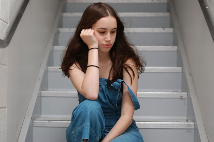 Young woman sitting on stairs looking thoughtful, representing woman taking dad to court over stolen inheritance case.