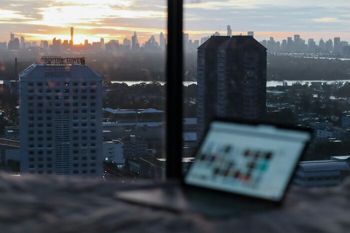 City skyline at sunset viewed from a window with a laptop, illustrating the best time to buy a plane ticket for cheap airfare.