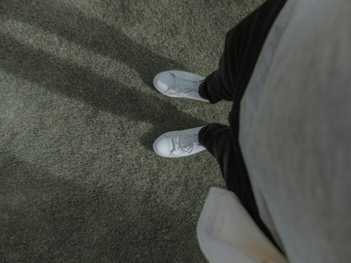 Person wearing white sneakers looking down at a green carpet illustrating big no no to do in your country concept.