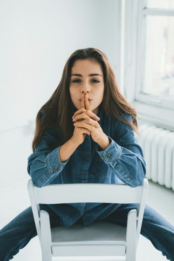 Young woman in denim sitting backward on chair, contemplative expression, reflecting on moments close friend revealed as jerk