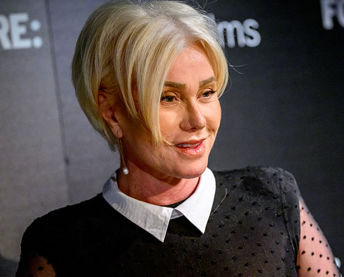 Sutton Foster in a black dress with pearl earrings, smiling at an event with a dark backdrop. Sutton Foster in a black dress with pearl earrings, smiling at an event with a dark backdrop.