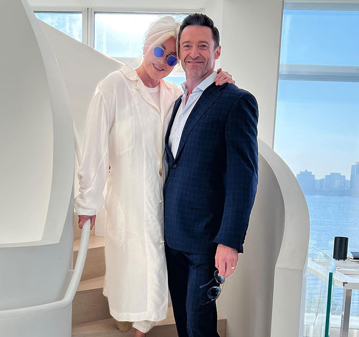 Hugh Jackman and Sutton Foster posing together on a staircase with a waterfront city view behind them. Hugh Jackman and Sutton Foster posing together on a staircase with a waterfront city view behind them.