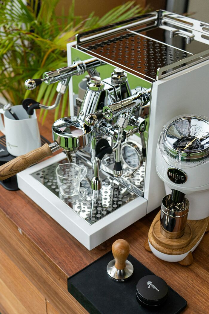 Close-up of a private resort worker's espresso machine setup featuring a grinder, tamper, and steaming wand on a wooden counter.