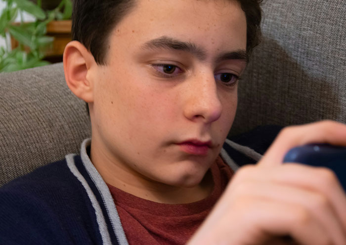 Teenage boy looking intently at smartphone, capturing emotions related to delivery room stories about child paternity issues.