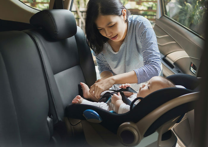 Mother securing baby in car seat, focusing on child paternity questions in delivery room stories.