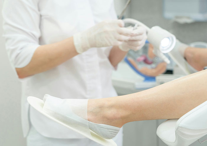 Medical professional wearing gloves preparing for delivery room procedure with patient’s leg positioned and covered in disposable foot covering.