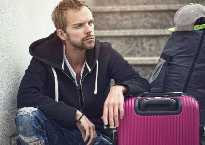 Man sitting on stairs next to luggage, looking thoughtful about delivery room stories when the child is not the father’s.