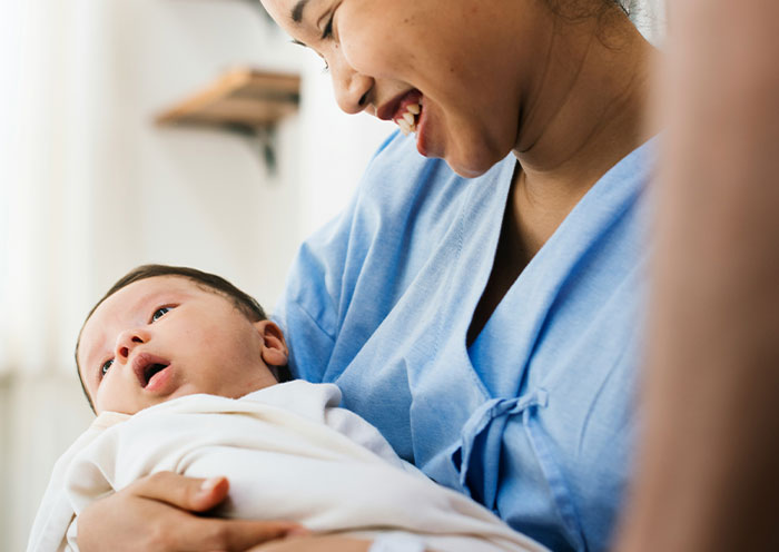 Mother in a delivery room holding newborn baby, smiling gently while bonding moments unfold after birth.