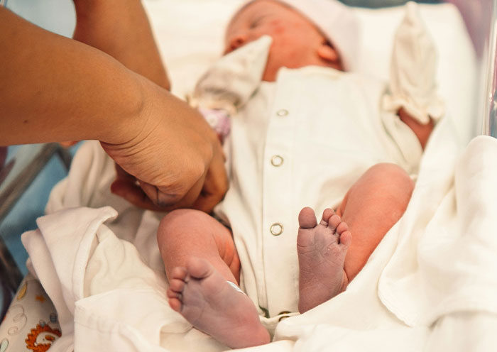 Newborn baby in delivery room with a caregiver, illustrating delivery room stories about paternity and childbirth surprises.