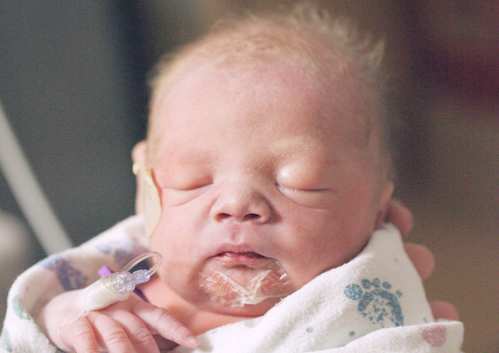 Newborn baby wrapped in a hospital blanket with medical tubes, symbolizing delivery room stories about paternity surprises.