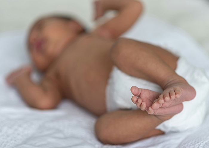 Newborn baby lying on a white blanket in a delivery room, focusing on the infant’s feet and legs.
