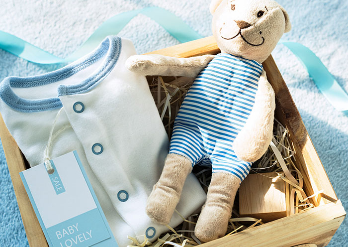 Newborn baby clothes and a soft teddy bear in a wooden box, symbolizing delivery room stories about paternity.