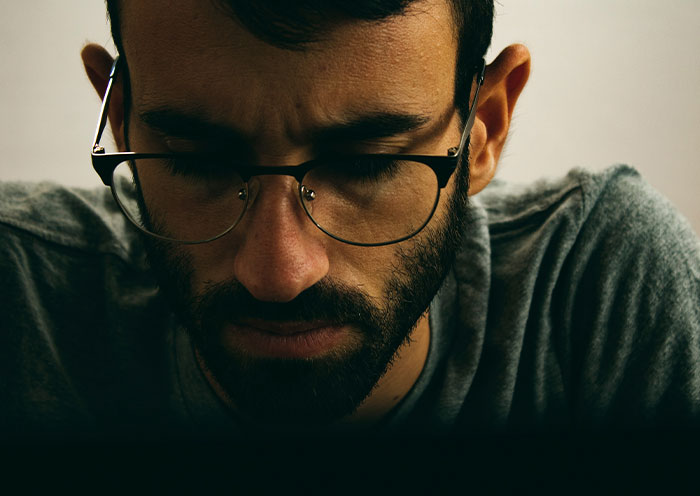 Man with glasses and beard looking down thoughtfully, illustrating delivery room stories when child is not the father's.