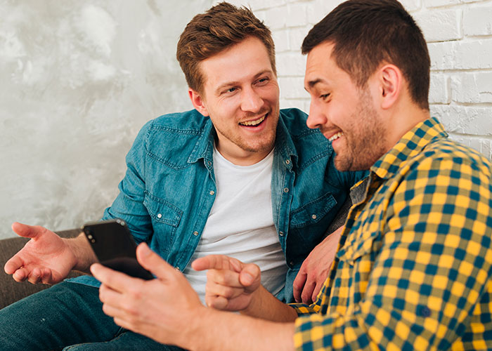 Two men having a friendly conversation as one shows his phone, discussing dating influencer-like women and reality check. Two men having a friendly conversation as one shows his phone, discussing dating influencer-like women and reality check.