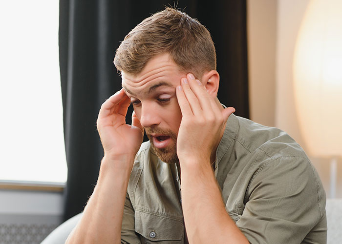 Man looks frustrated while holding his head indoors, reflecting on dating influencer-like women and a friend's reality check. Man looks frustrated while holding his head indoors, reflecting on dating influencer-like women and a friend's reality check.