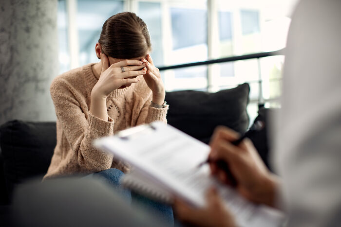 Woman covering her face in a therapy session with therapist taking notes, illustrating therapists judging moments.