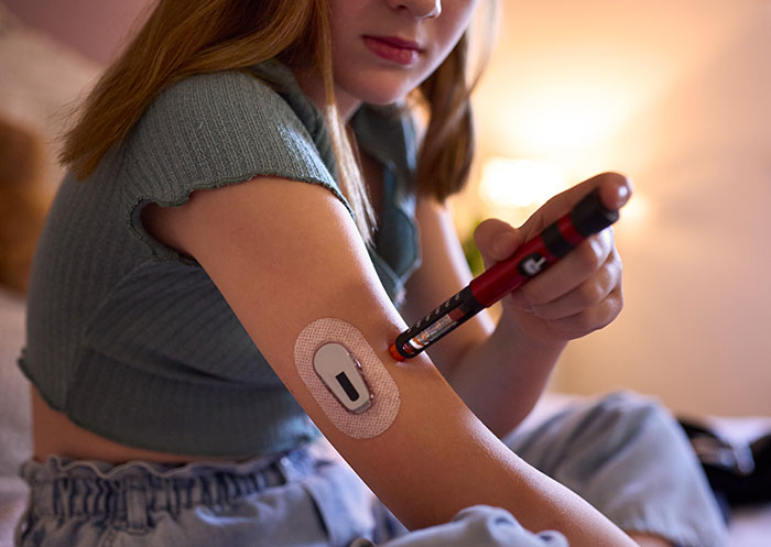 Woman administering insulin with a pen, prioritizing health over sister&rsquo;s wedding photo aesthetic concerns.