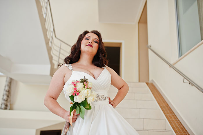 Woman in wedding dress holding bouquet, standing on stairs, symbolizing health concerns and wedding photo aesthetic conflict.