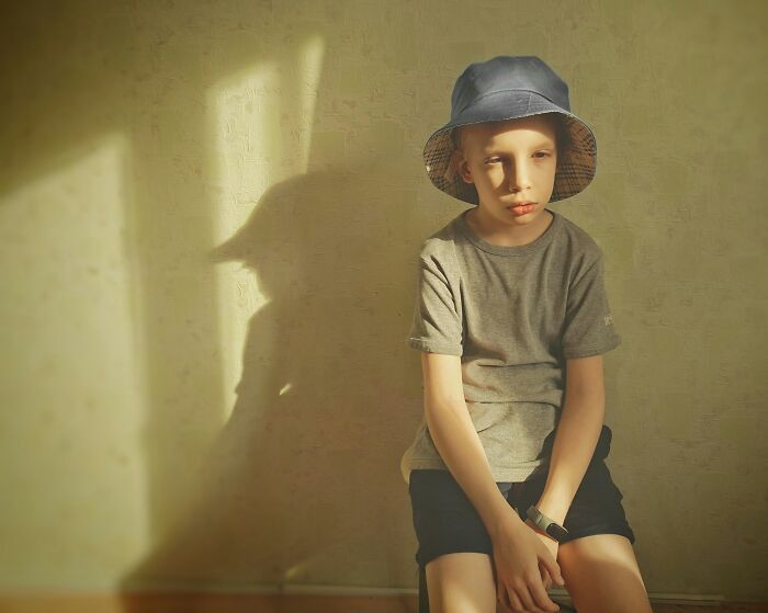 Young boy in casual clothes and hat sitting alone, illustrating casual and harmless looking habits potentially damaging long term.