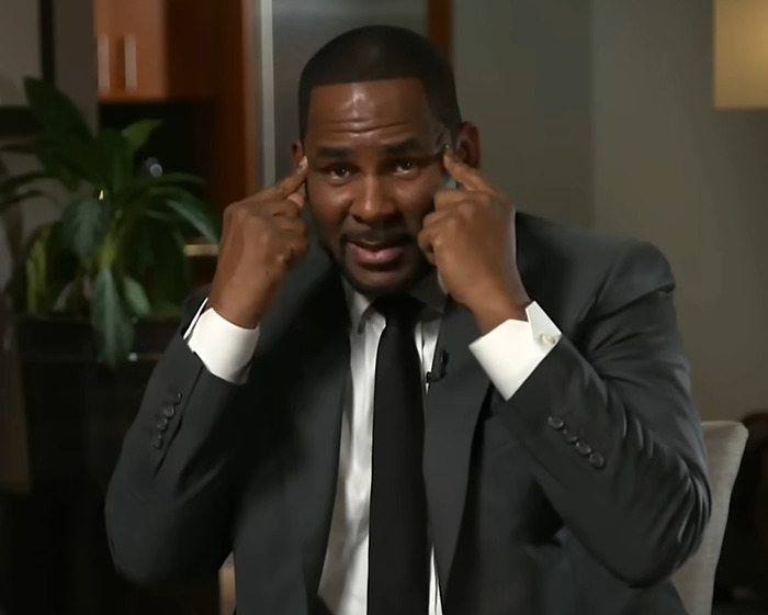 Disgraced rapper R Kelly in an interview, wearing a suit and gesturing to his head, discussing prison overdose and assassination plot. Disgraced rapper R Kelly in an interview, wearing a suit and gesturing to his head, discussing prison overdose and assassination plot.