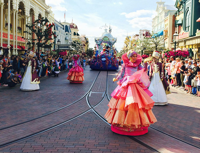 Performers in colorful costumes entertain crowds during a Disneyland wedding interrupted by staff over the young bride's age.