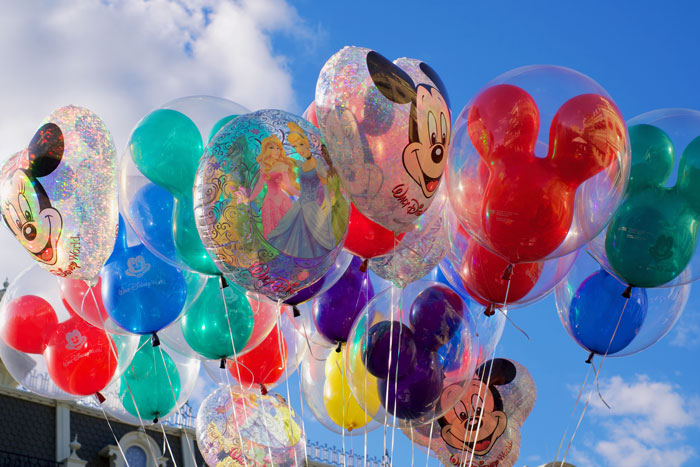 Colorful Disneyland balloons featuring Mickey Mouse and princess designs floating against a bright blue sky at a theme park. Colorful Disneyland balloons featuring Mickey Mouse and princess designs floating against a bright blue sky at a theme park.