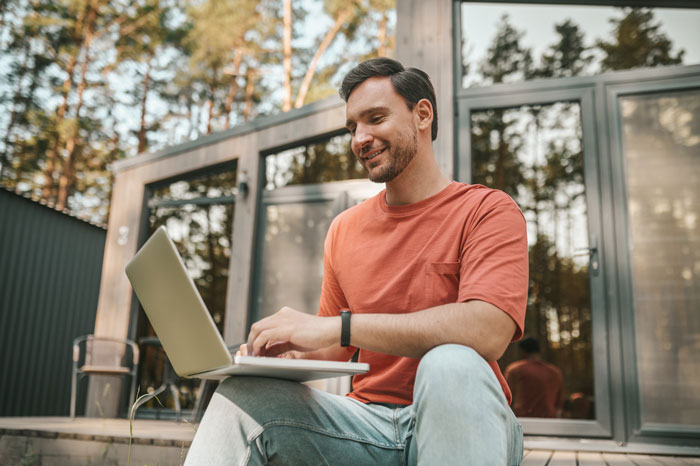 Man using laptop outdoors, smiling as he types, representing guy seeking job referral after divorce and ghosting friend.