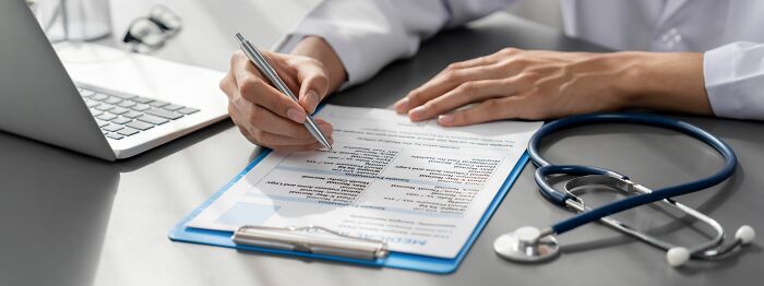 Doctor filling out a medical form on a clipboard with a stethoscope and laptop nearby, symbolizing hidden family secrets.