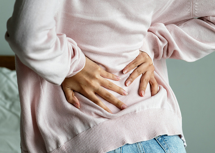 Person wearing pink sweater holding lower back in pain, illustrating medical conditions that surprised doctors.