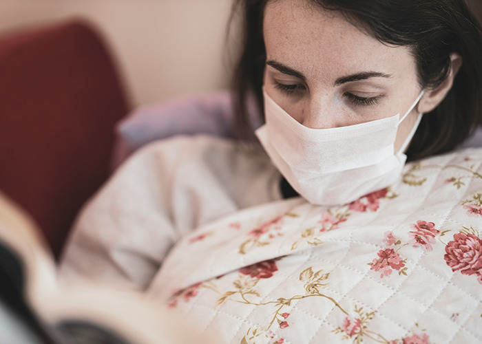 Woman wearing a mask and wrapped in a floral blanket, appearing unwell and reflecting on medical conditions that surprised doctors.
