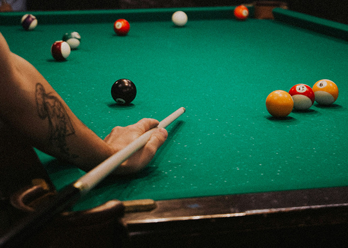 Person with a tattoo aiming a pool cue at billiard balls on a green felt table, illustrating a bizarre medical case theme.