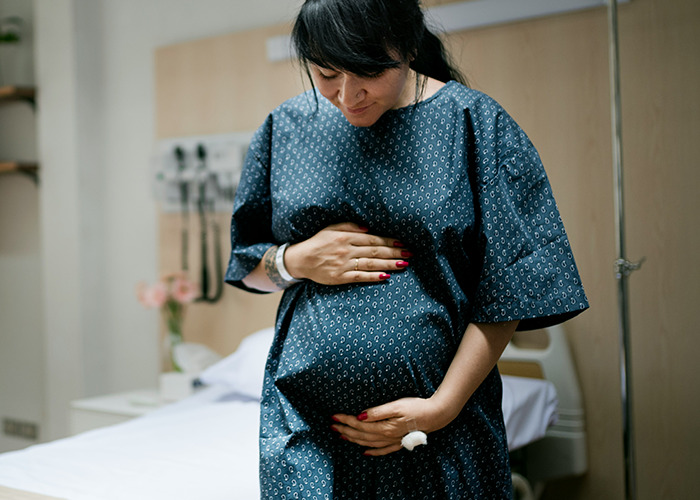 Pregnant woman in hospital gown holding her belly, representing bizarre medical cases involving skin conditions.