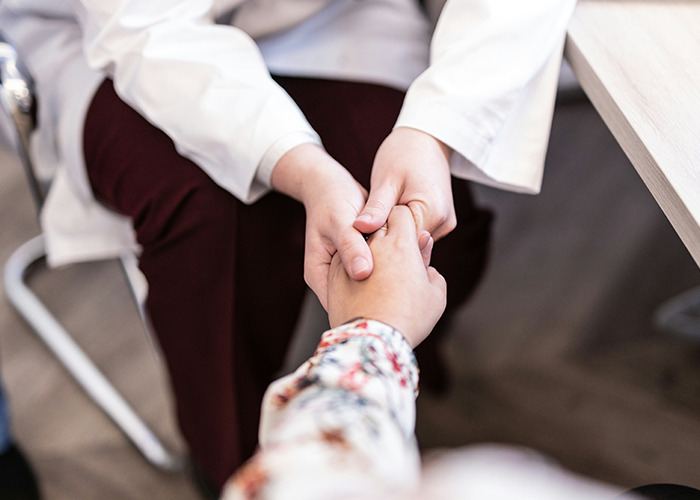 Doctor wearing white coat holding patient's hand showing care and support during consultation about medical conditions.