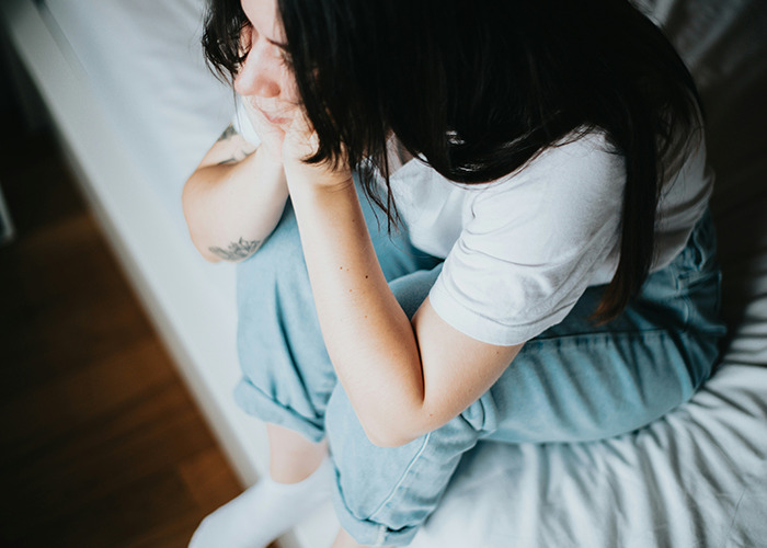 Young woman sitting on bed, holding her face in hands, depicting distress related to bizarre medical cases involving skin.