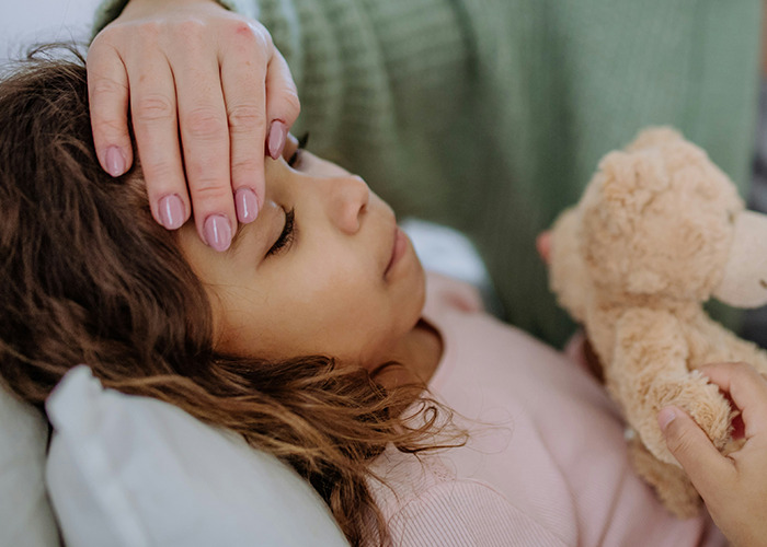 Child lying down with eyes closed, being comforted by hand on forehead, highlighting bizarre medical cases involving skin.