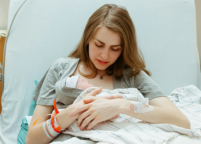 Young mother in hospital bed holding newborn baby wrapped in blanket, representing medical conditions that surprised doctors.