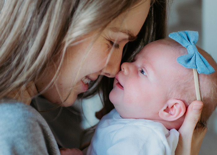 Mother smiling gently at her newborn baby girl wearing a blue bow headband, highlighting tender medical care moments.