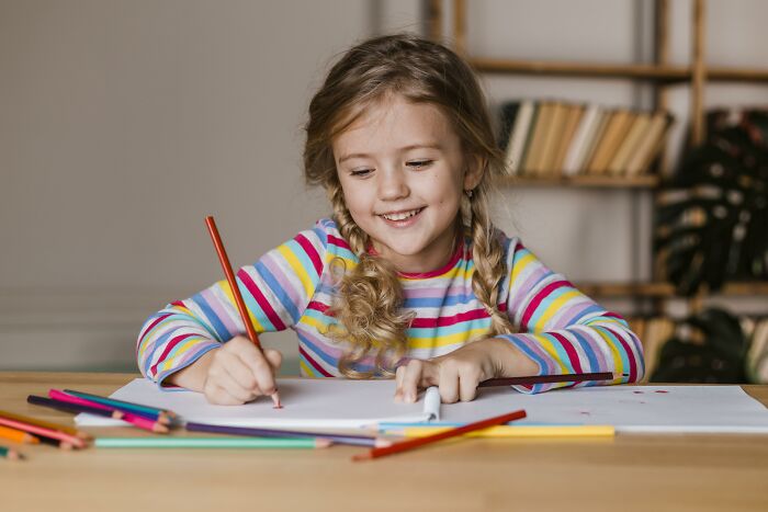Young girl with braided hair using colored pencils to express creative freedom in art at a wooden table.