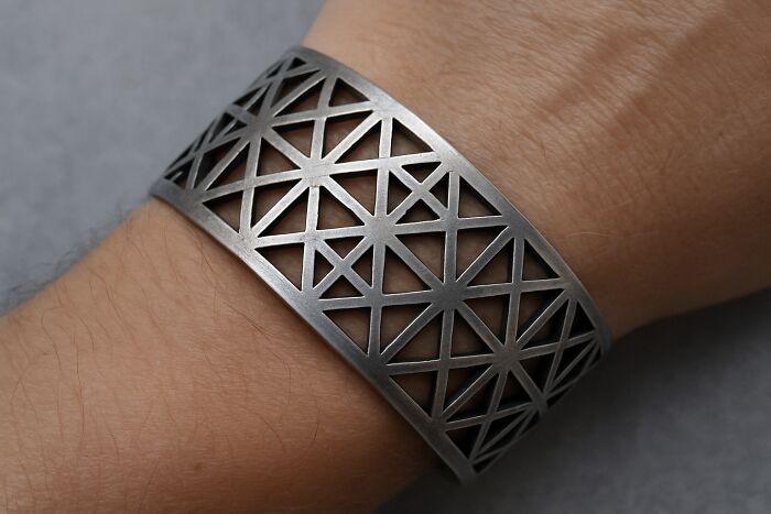 Metal bracelet with geometric cut-out design worn on wrist, showcasing creative freedom in art and design.