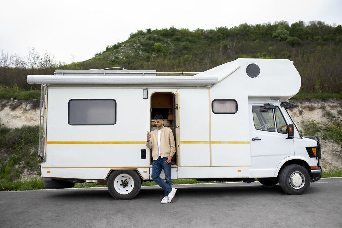 Man standing outside a white campervan by a hillside, symbolizing creative freedom in art teachers online discussions.