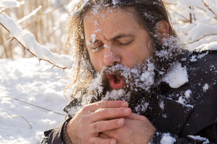 Man with snow-covered beard and hair warming his hands in snowy outdoor setting, showing unhinged creative freedom.