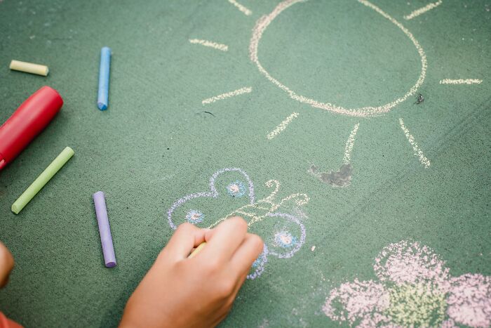 Child drawing colorful chalk butterfly and sun on green chalkboard showcasing kids creative freedom in art teachers online session.